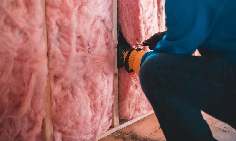 Contractor installing pink fiberglass insulation batts in a wall cavity